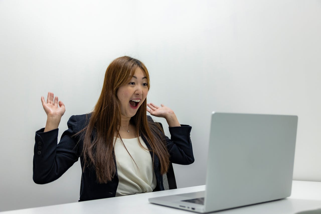 gallery-5 A joyful businesswoman expresses excitement while working on her laptop in a modern office.