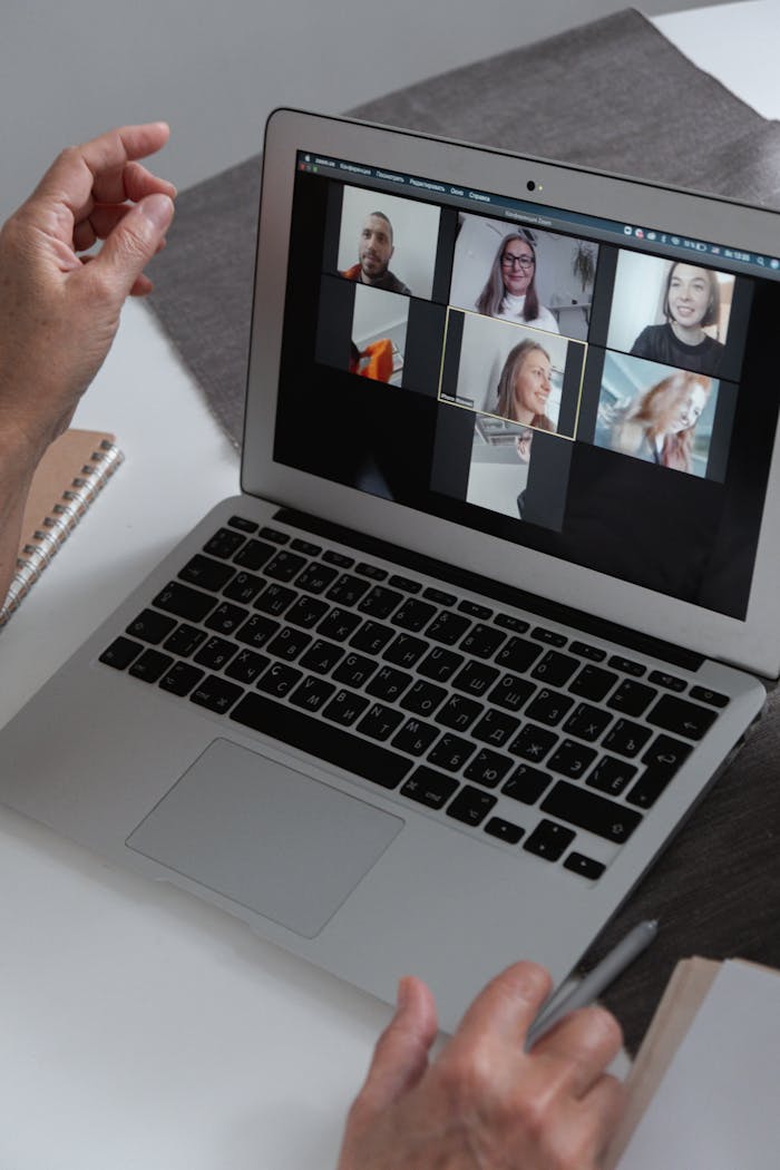 ours-journey Hands at a laptop showing a group video call in a home office setting.